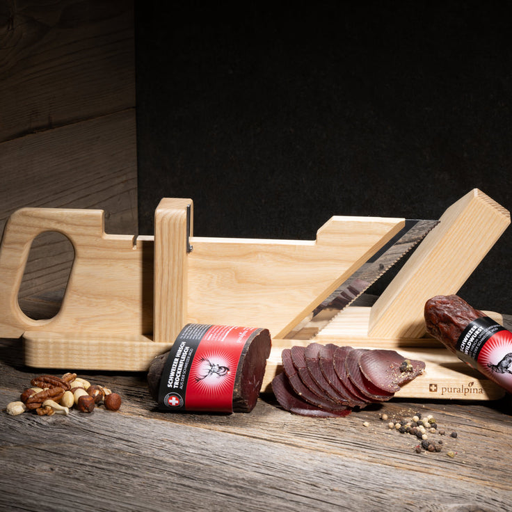 Trancheuse à salami de Puralpina avec saucisse de sanglier suisse, venaison séchée et charcuterie sur une table en bois
