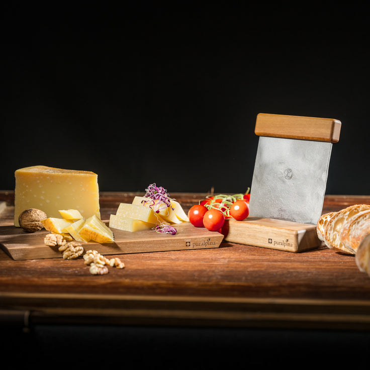 Puralpina Käseschneider aus Nussbaumholz mit Käse, Tomaten, Brot und Baumnüssen angerichtet