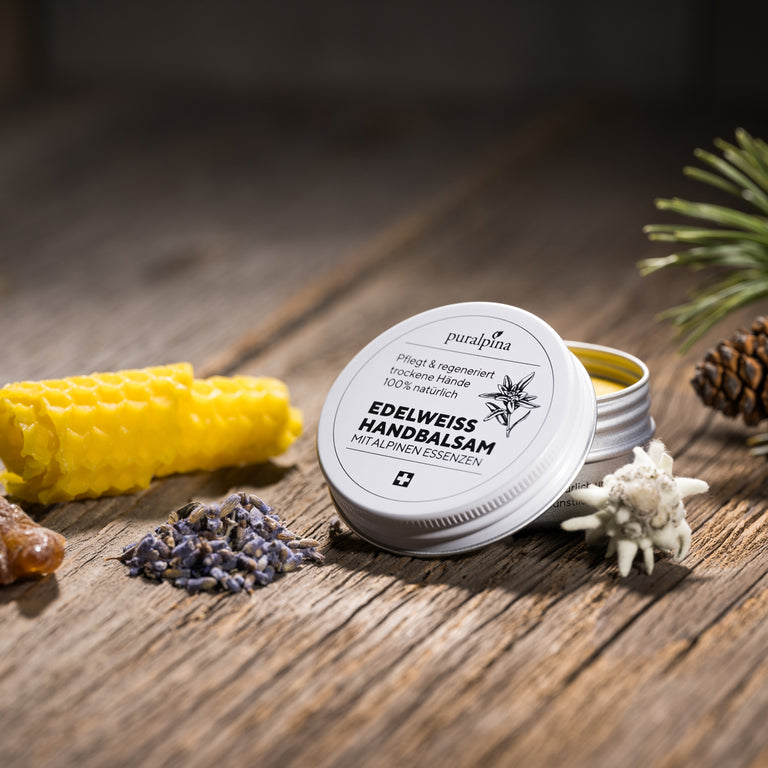 puralpina Edelweiss Handbalsam in geöffneter Dose auf Holztisch mit Bienenwachs und Alpenblüten