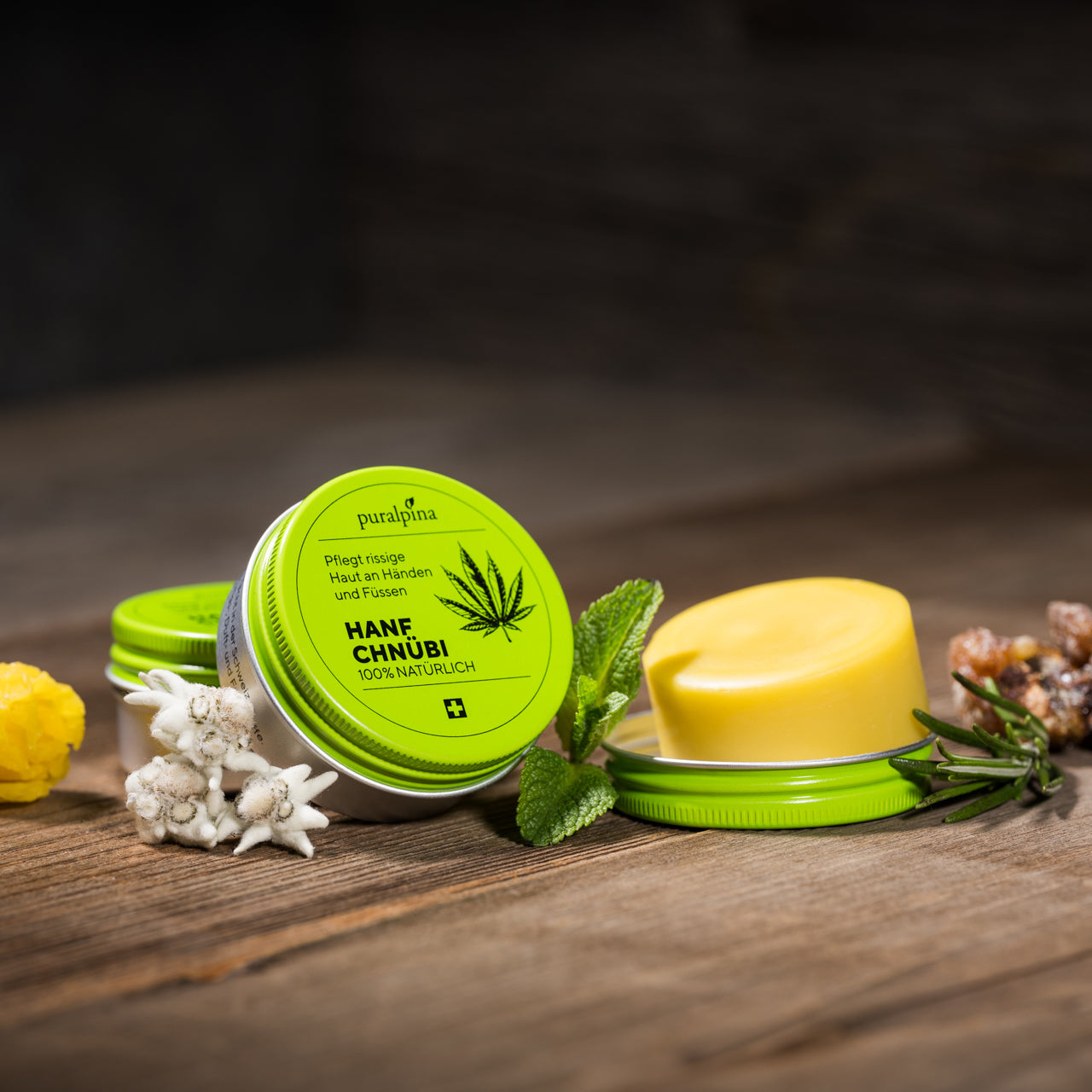 puralpina Hanf Chnübi mit geöffneter Dose, Produkt, Edelweiss und Kräutern auf Holztisch