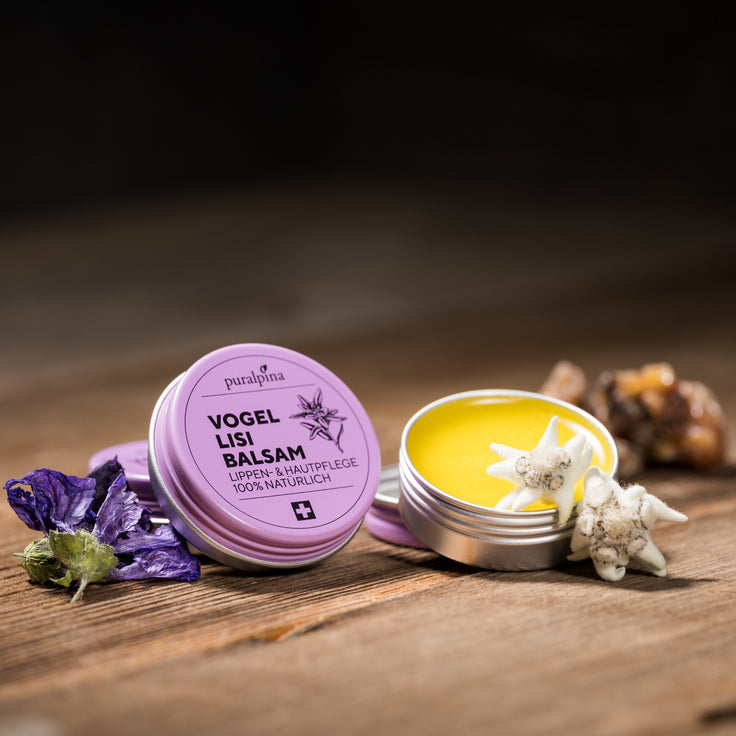 Geöffnete und geschlossene Dose puralpina Vogellisi Balsam mit violetten Blüten und Edelweiss auf Holztisch